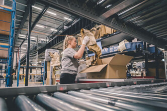 An employee loads a carton with filling material for an order