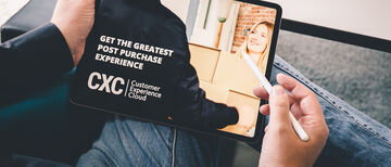 Wir blicken über eine Schulter auf ein Tablet, auf dem die Customer Experience Cloud mit dem Slogan "Get the greatest post purchase experience" beworben wird
