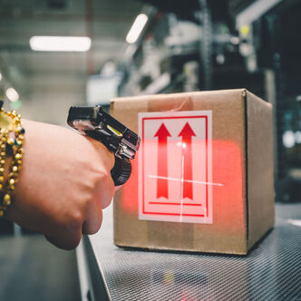 Ein Arvato-Mitarbeiter scannt im Rahmen des B2B-Fulfillments ein Paket mit einem Fingerscanner