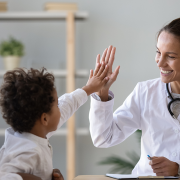 a little boy on his father's arm gives a smiling pediatrician a high five