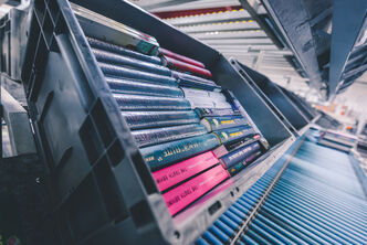 a filled transport box with books on a roller conveyor belt and further transport boxes