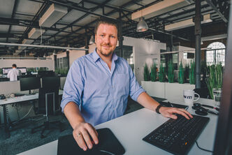 a call center service agent standing in front of a desktop wearing a blue shirt