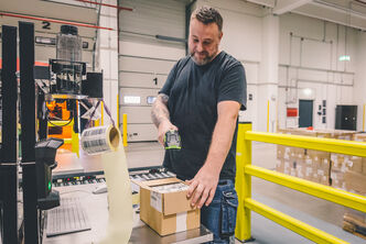 Mitarbeiter steht an einer Packstation und scannt Barcodes
