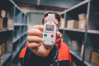 An Arvato employee holds a temperature monitoring device up to the camera
